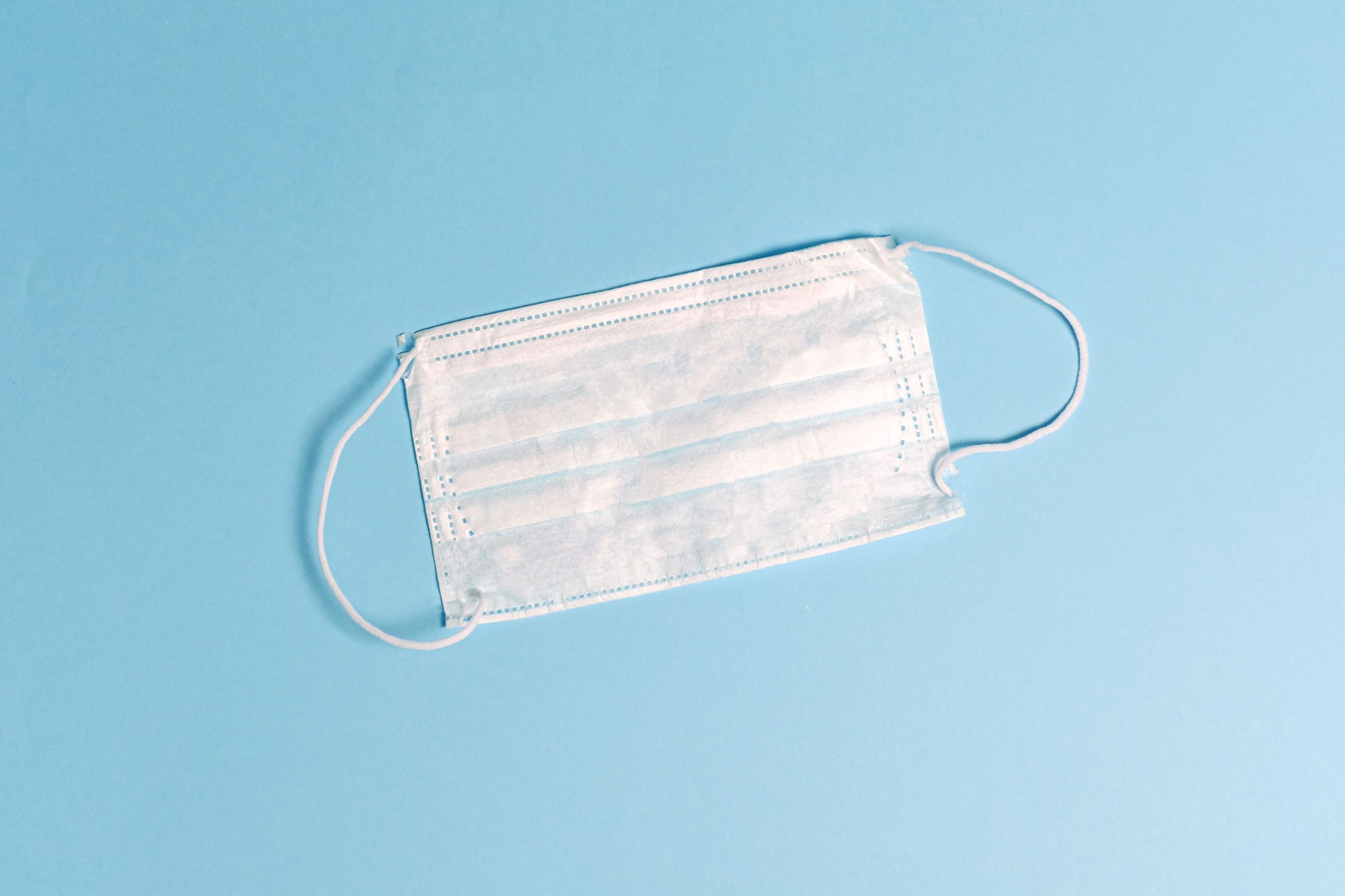 A white surgical mask lies against a blue background